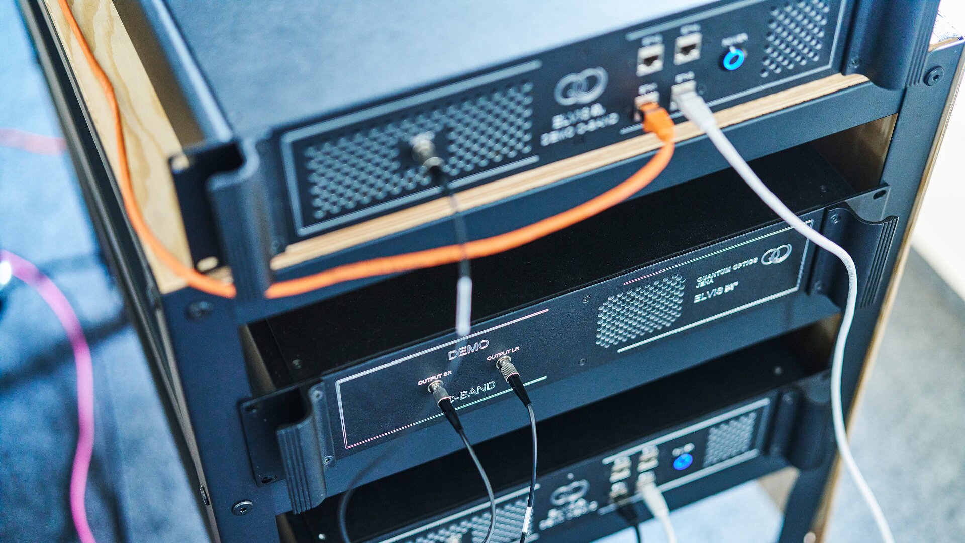Server-Rack mit mehreren Netzwerkgeräten und an verschiedene Ports angeschlossenen Kabeln, darunter orangefarbene, schwarze und weiße Ethernet-Kabel, in einer Technologie- oder Rechenzentrumsumgebung.