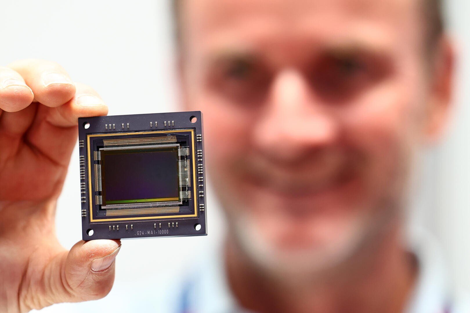 Eine Person hält einen Computerchip oder Sensor hoch und konzentriert sich auf die Hardware, die sie zwischen ihren Fingern hält. Ihr Gesicht ist im Hintergrund unscharf.