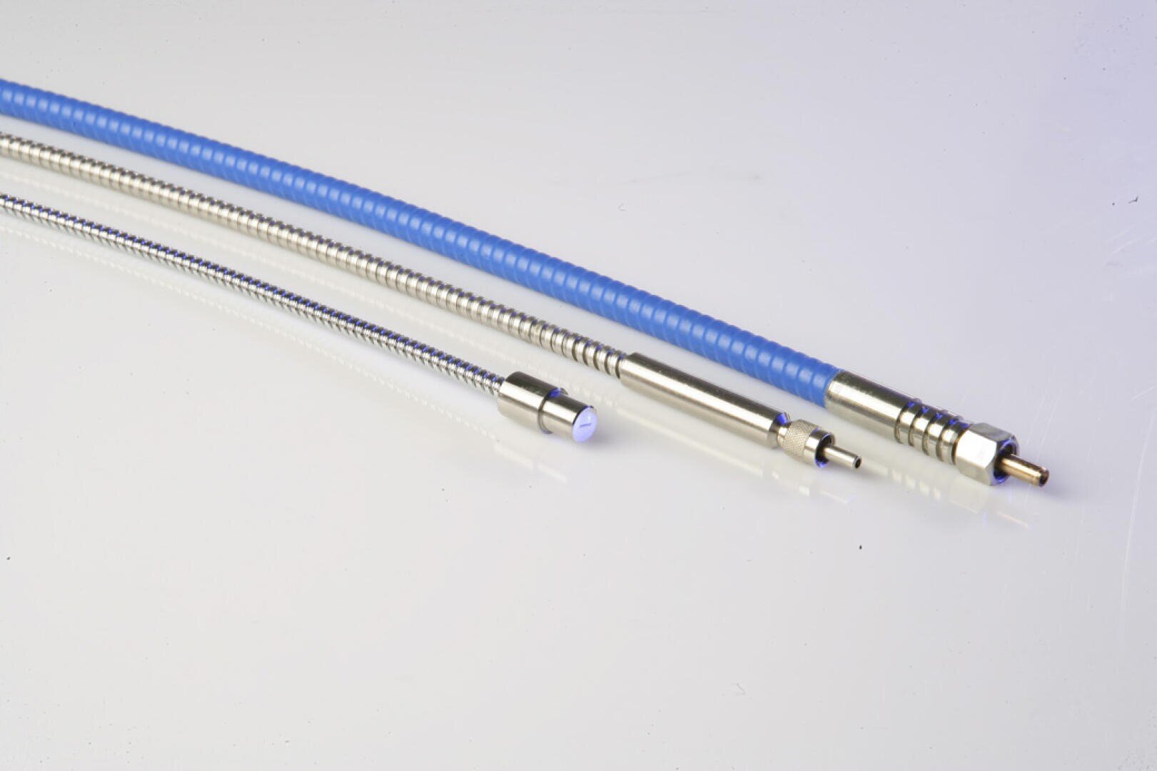 Three flexible, metallic cables with silver connectors and a blue outer covering on one cable, all laid out on a white surface.