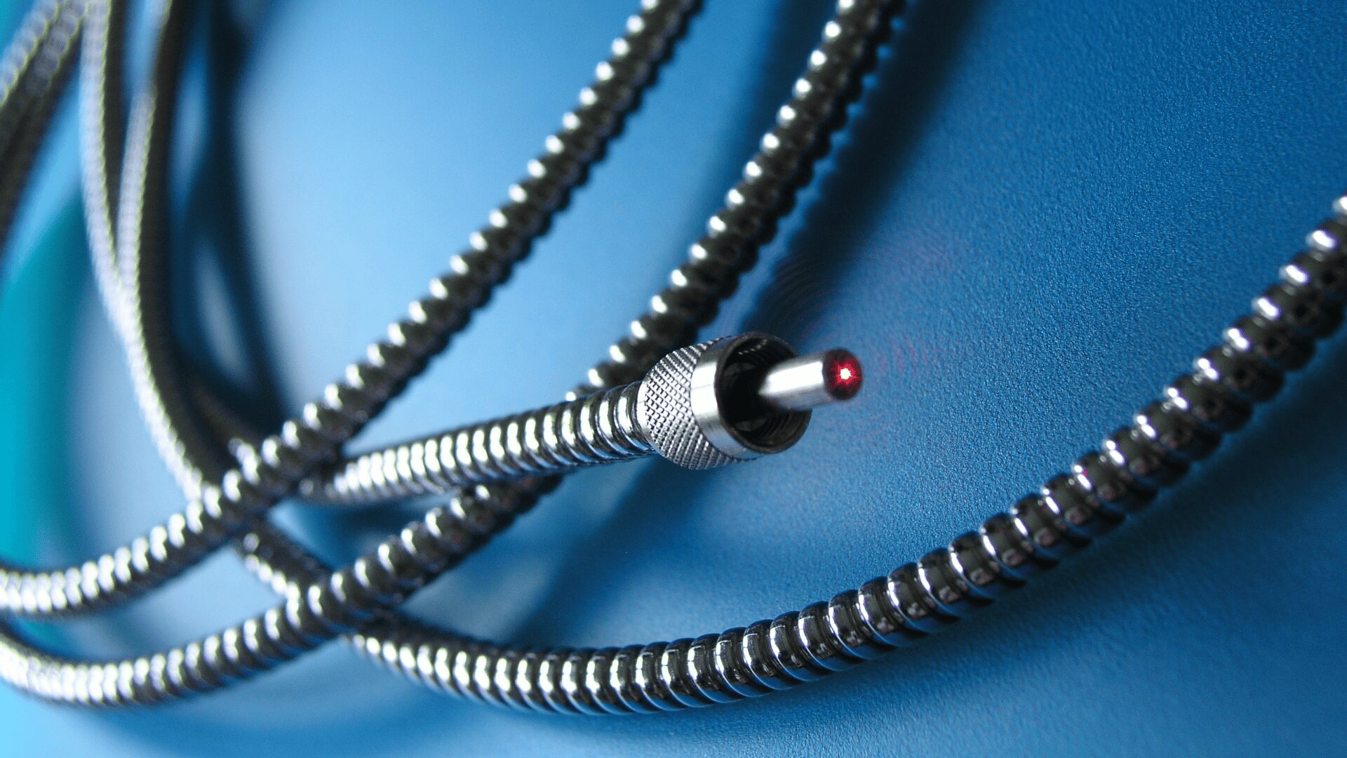 Close-up of a fiber optic cable with a glowing red light at the tip, coiled loosely on a smooth blue surface.