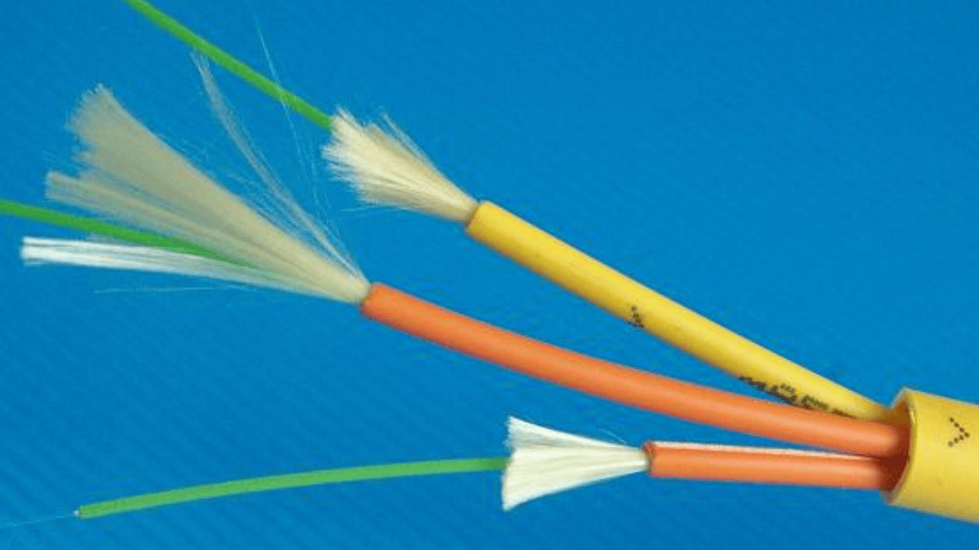 Close-up of a yellow fiber optic cable with its outer sheath partially stripped, exposing inner orange and green cables, along with white strengthening fibers, against a blue background.